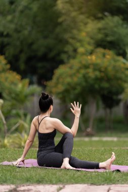Spor kıyafetli orta yaşlı, kendinden emin bir Asyalı kadın sabahları arka bahçede yoga minderinde yoga egzersizi yapıyor. Genç bir kadın doğa parkında yoga egzersizi yapıyor.