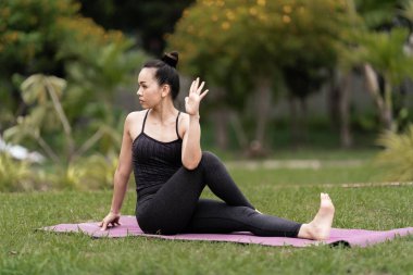 Spor kıyafetli orta yaşlı, kendinden emin bir Asyalı kadın sabahları arka bahçede yoga minderinde yoga egzersizi yapıyor. Genç bir kadın doğa parkında yoga egzersizi yapıyor.