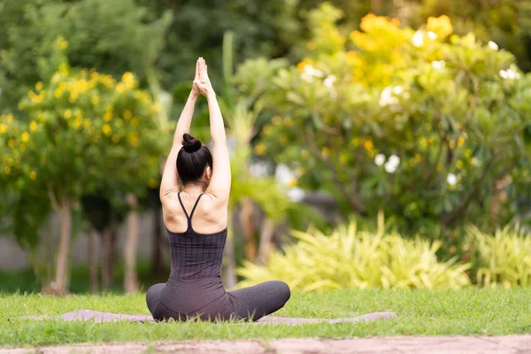 Spor kıyafetli orta yaşlı, kendinden emin bir Asyalı kadın sabahları arka bahçede yoga minderinde yoga egzersizi yapıyor. Genç bir kadın doğa parkında yoga egzersizi yapıyor.