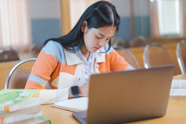 İnternette okuyan, kitap okuyan, üniversite kütüphanesinde dijital tablet ya da dizüstü bilgisayar kullanan stresli bir Asyalı üniversite öğrencisi.