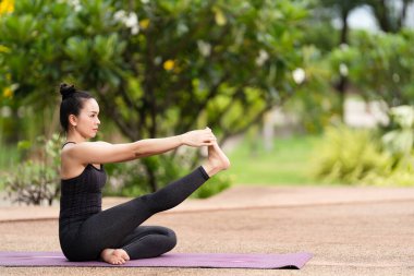 Spor kıyafetli orta yaşlı, kendinden emin bir Asyalı kadın sabahları arka bahçede yoga minderinde yoga egzersizi yapıyor. Genç bir kadın doğa parkında yoga egzersizi yapıyor.