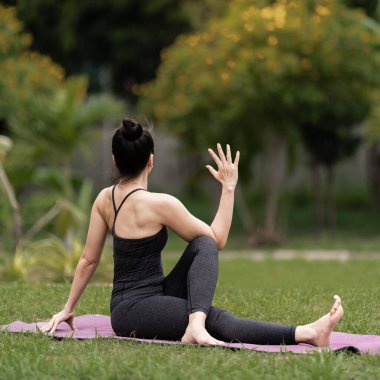Spor kıyafetli orta yaşlı, kendinden emin bir Asyalı kadın sabahları arka bahçede yoga minderinde yoga egzersizi yapıyor. Genç bir kadın doğa parkında yoga egzersizi yapıyor.