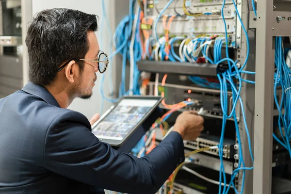 Ağın sunucu odasındaki ağ kablosuna bağlı çalışan genç bir ağ teknisyeninin stok fotoğrafı. Ağ sunucu odasında çalışan bilişim mühendisi