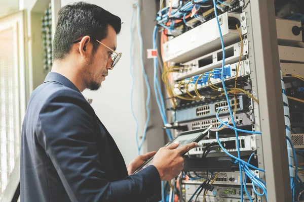 Stock photo of a young network technician holding tablet working to connecting network cables in server cabinet in network server room. IT engineer working in network server room