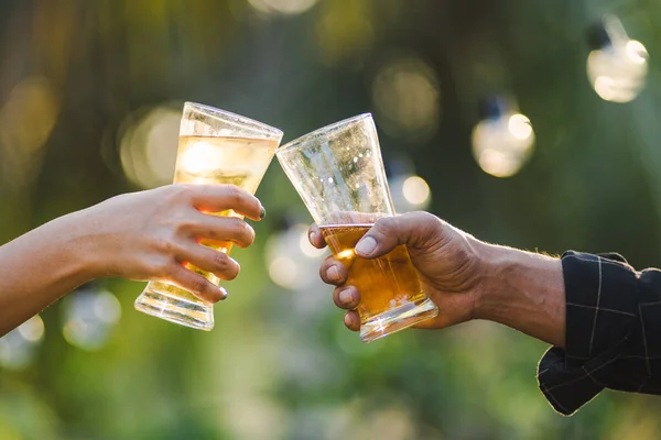 Cropped shot of people holding beer glasses celebrating in the summer camping party outdoor. Friends clinking bottle of beer during camping outdoor