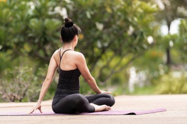 Spor kıyafetli orta yaşlı, kendinden emin bir Asyalı kadın sabahları arka bahçede yoga minderinde yoga egzersizi yapıyor. Genç bir kadın doğa parkında yoga egzersizi yapıyor.