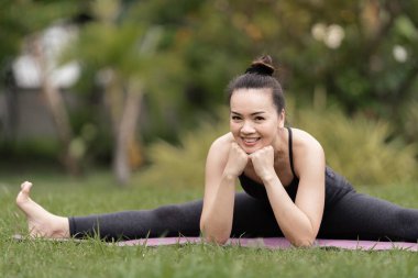 Spor kıyafetli orta yaşlı, kendinden emin bir Asyalı kadın sabahları arka bahçede yoga minderinde yoga egzersizi yapıyor. Genç bir kadın doğa parkında yoga egzersizi yapıyor.