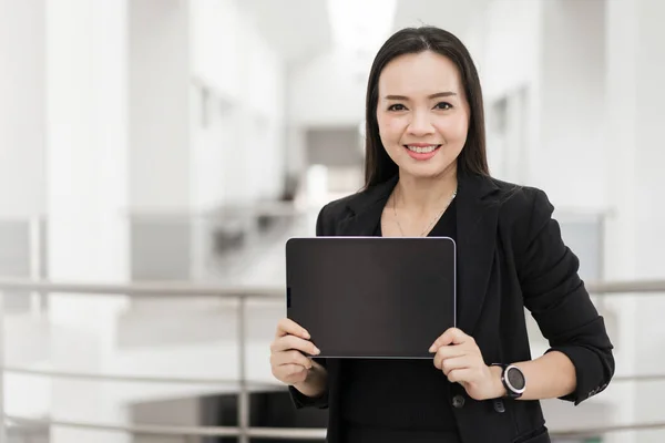オフィスビル内に設置されたデジタルタブレットを活用し ビジネス志向のコンセプトを表現したブラックビジネススーツ姿のアジア人ビジネスマンの自信作 — ストック写真