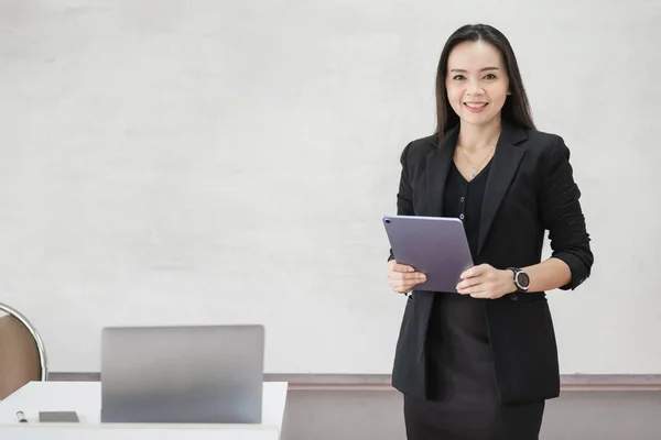 教室で現代語を教えるために デジタルタブレットとラップトップで統一された黒のビジネススーツで自信を持って陽気なアジアの女性教師のストックフォト肖像画 — ストック写真