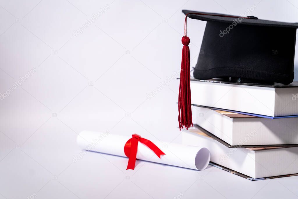 Stock photo of a graduation cap mortar board and diploma certificate isolated on white background with negative copy space to add text. Graduation hat with diploma on table against white background