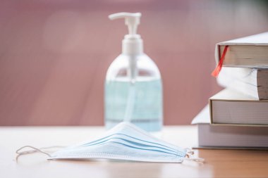 Masadaki kitap yığını COVID-19 salgınını önlemek için yüz maskesi ve dezenfektan sıvısı ile. COVID-19 döneminde eğitim