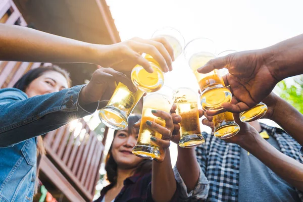 Cropped shot of people holding beer glasses celebrating in the summer camping party outdoor. Friends clinking bottle of beer during camping outdoor