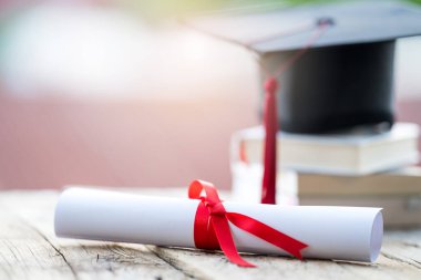 Mezuniyet şapkasının veya havan tahtasının ve diploma diplomasının masadaki seçici odak noktasını kapat