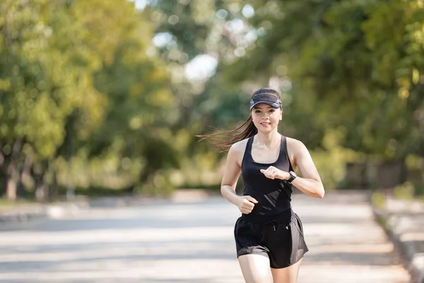 A healthy happy Asian woman runner in black sport outfits jogging in the natural city park under evening sunset