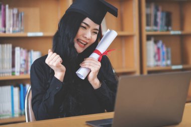 Genç Asyalı bayan üniversite mezunu bir video aracılığıyla sanal mezuniyeti kutluyor.