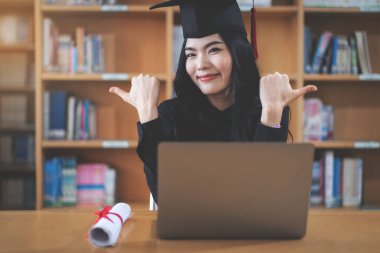 Genç Asyalı bayan üniversite mezunu bir video aracılığıyla sanal mezuniyeti kutluyor.