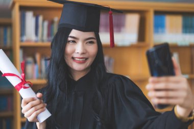 Mezuniyet elbisesi ve havan panosu mezuniyetini sanal bir mezuniyet töreniyle kutluyor. Mezuniyet gününde evde mutlu bir bayan öğrenci. Çevrimiçi eğitim kavramı