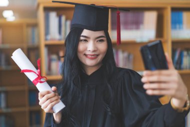 Mezuniyet elbisesi ve havan panosu mezuniyetini sanal bir mezuniyet töreniyle kutluyor. Mezuniyet gününde evde mutlu bir bayan öğrenci. Çevrimiçi eğitim kavramı