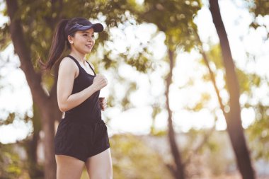 Mutlu gülümseyen Asyalı kadın güzel bir yaz gününde şehir parkında koşuyor. Mutlu, rahat, olgun bir kadın aktif ve sağlıklı bir yaşam tarzı için koşuyor.