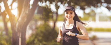 Mutlu gülümseyen Asyalı kadın güzel bir yaz gününde şehir parkında koşuyor. Mutlu, rahat, olgun bir kadın aktif ve sağlıklı bir yaşam tarzı için koşuyor.