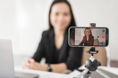 Yetişkin Asyalı kadın kolej öğretmeni evdeki öğrencilere video konferansı aracılığıyla ders veriyor. Gülümseyen Asyalı bayan öğretmen öğrencilerle video görüşmesi yapıyor..