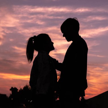 Renkli bir günbatımı gökyüzünün altında birbirine bakan genç bir çiftin silueti, sevgiyi, sıcaklığı ve bağlantıyı ifade ediyor. Romantik ruh hali Güzel bulutlar ve altın akşam ışığı.