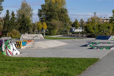 Wroclaw, Poland- 24 Ekim 2025: Rampaların üzerinde canlı graffiti ile kaykay parkı, yeşillik ile çevrili, açık hava aktiviteleri ve spor meraklılarını canlı atmosferin tadını çıkarmaya davet ediyor