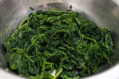 Mutfak tezgahında taze, sıkılmış ıspanak yapraklarıyla dolu paslanmaz çelik karıştırma kabı. Terbiye edilmeye ya da sağlıklı bir ev yapımı sebze yemeği malzemesi olarak kullanılmaya hazır..