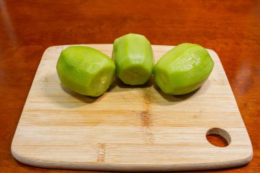 Üç soyulmuş yeşil kiwifruit 'in yakın plan fotoğrafı açık tahta kesme tahtasının üzerinde duruyor. Pürüzsüz parlak yüzey ve kesik uçları sıcak kahverengi bir tabloda görünür, metin için kopyalama alanı ile.