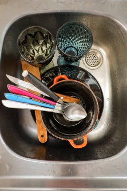 Kirli tabaklar, tencere, bardaklar ve kullanımdan sonra paslanmaz çelik lavaboya konan renkli mutfak aletleri.