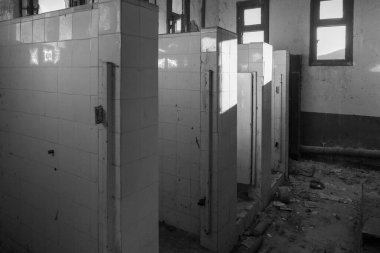 Siyah ve beyaz fotoğraf, harap olmuş bir tuvalette kentsel bozulmayı yakalıyor. Sessizlik, kayıp zaman ve unutulmaz boşluk temalarını çağrıştırıyor..