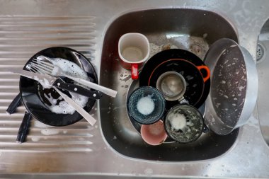 Mutfak lavabosunda sabunla kaplanmış temiz tabak ve bardaklardan oluşan bir koleksiyon. Temizliği ve günlük ev işlerini temsil ediyor..