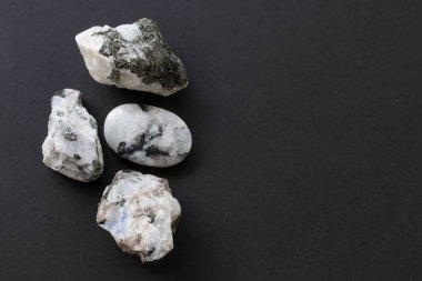 Siyah arka planda sergilenen ham ay taşı kristalleri. Sağlık, metafizik ve mineral içeriği için ideal.