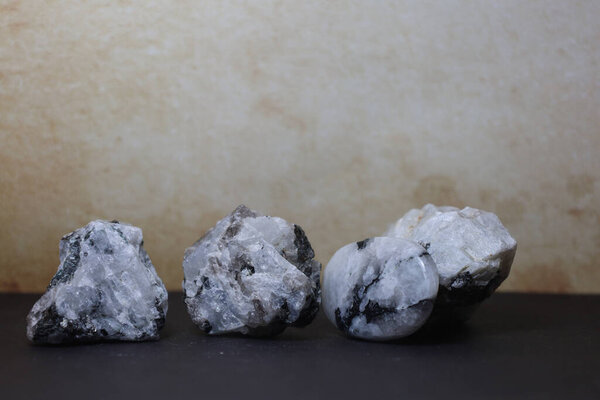 A collection of moonstone crystals in both raw and polished form, arranged on a dark studio surface.