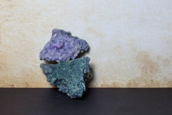 İki botryoidal üzüm agat mineral örnekleri mor ve yeşil renklerde yumuşak bej bir arkaplan üzerine istiflenmiştir.