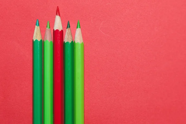 Renk karşıtlığını ve modern minimal tasarımı gösteren, koyu kırmızı arkaplan üzerine paralel olarak sıralanmış yeşil ve kırmızı renkli kalemlerin stüdyo görüntüsü.