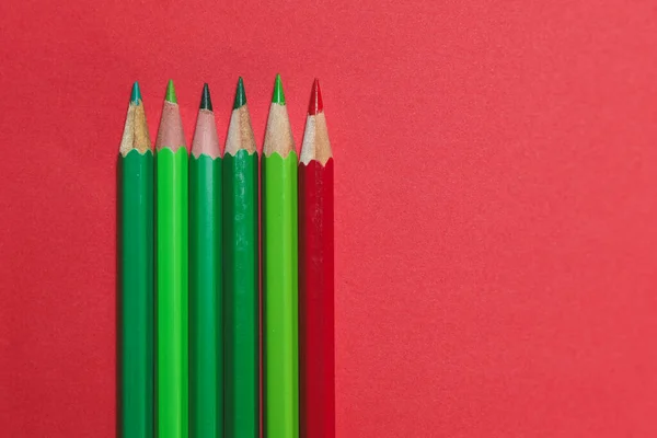 Renk karşıtlığını ve modern minimal tasarımı gösteren, koyu kırmızı arkaplan üzerine paralel olarak sıralanmış yeşil ve kırmızı renkli kalemlerin stüdyo görüntüsü.