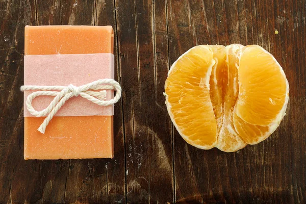 Kırsal ahşap üzerinde taze soyulmuş narenciye ile sergilenen el yapımı turuncu sabun, spa markası, eko yaşam tarzı pazarlaması ve organik cilt bakımı kampanyaları için ideal..