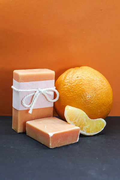 Canlı turuncu arka planda taze portakal ve narenciye dilimleri sergilenen el yapımı turuncu sabunlar. Doğal cilt bakımı konsepti organik bileşenleri vurgular