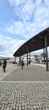 Modern ve zarif mimarisi olan bir meydan manzarası, ikonik figürlerin heykelleri. Şehir merkezindeki bulutlu gökyüzü bir huzur ve tefekkür hissi taşır..