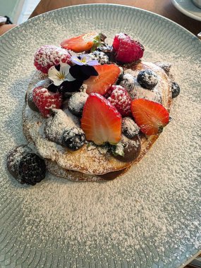 Çikolatalı leziz krepler, çilek, yabanmersini ve ahududu gibi taze meyveler, yenilebilir çiçeklerle ve toz şekerle bitirilmiş..