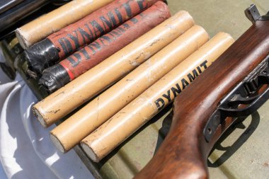Askeri yüzeyde dinamit sopaları ve tüfek var.