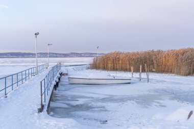 Donmuş rıhtım ve buzlu gölde kamışlı tekne, Macaristan 'ın Balaton Gölü' nde.