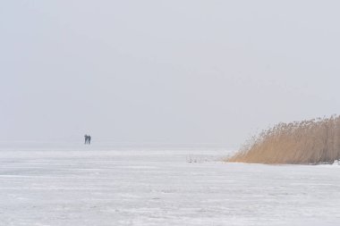 Donmuş bir gölün buzunun üzerindeki minimalist kış manzarası. İki uzak insanla.