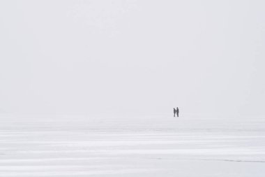 Donmuş bir gölün buzunun üzerindeki minimalist kış manzarası. İki uzak insanla.