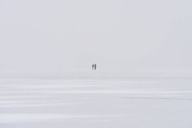 Donmuş bir gölün buzunun üzerindeki minimalist kış manzarası. İki uzak insanla.