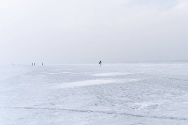 Kış sislerindeki insanlar donmuş bir gölün buzunda