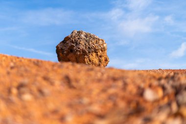 Terk edilmiş bir boksit madeninde parlak turuncu renkte, arka planda mavi gökyüzü olan aşınmış boksit kayası.