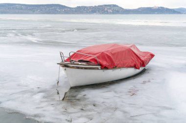 Donmuş kırmızı beyaz tekne Macaristan 'ın Balaton şehrinde kışın buzlu göle demirledi.
