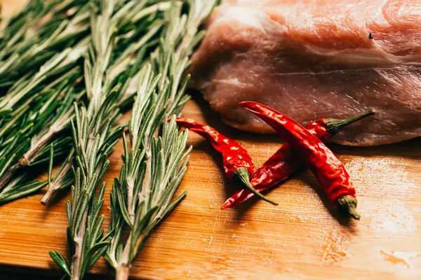 Ωμό κρέας, κλαδάκι δεντρολίβανο και κόκκινη καυτερή πιπεριά σε ανοιχτόχρωμο φόντο ξύλινη — Φωτογραφία Αρχείου